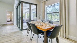 Een eetruimte met een houten tafel voor zes personen, zwarte stoelen en uitzicht door grote glazen deuren op een terras.