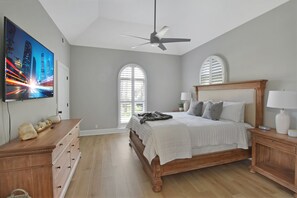 A bedroom with a bed, nightstands, a TV, a ceiling fan, and large windows. - Tabby Cottage: 3  BR, 3.5  BA House in Jekyll Island, Sleeps 6 (Jekyll Island)