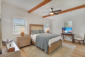 A bedroom with a bed, nightstands, a TV, and a ceiling fan. - Tabby Cottage: 3  BR, 3.5  BA House in Jekyll Island, Sleeps 6 (Jekyll Island)