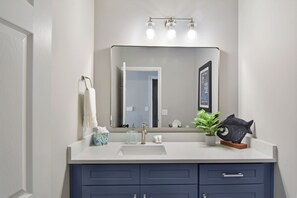 A bathroom with a white sink, a large mirror, and a blue vanity with drawers. - Tabby Cottage: 3  BR, 3.5  BA House in Jekyll Island, Sleeps 6 (Jekyll Island)