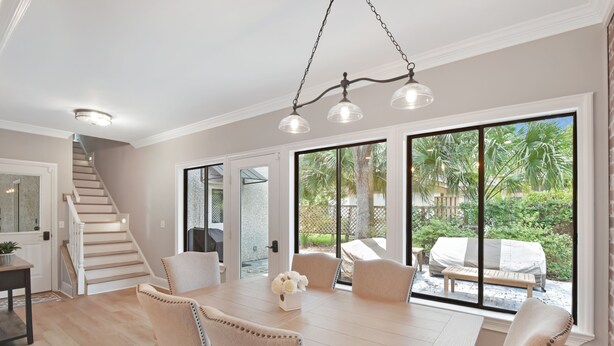 A dining area with a wooden table, beige chairs, and a chandelier. - Tabby Cottage: 3  BR, 3.5  BA House in Jekyll Island, Sleeps 6 (Jekyll Island)
