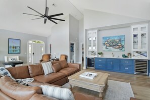 A spacious living room with a brown leather sofa, a wooden coffee table, and a ceiling fan. - Tabby Cottage: 3  BR, 3.5  BA House in Jekyll Island, Sleeps 6 (Jekyll Island)