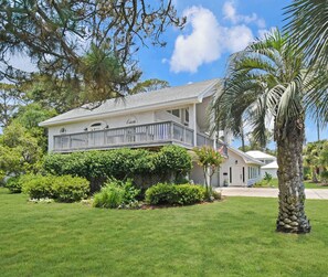 A two-story house with a balcony, surrounded by well-maintained lawns and tropical plants. - Tabby Cottage: 3  BR, 3.5  BA House in Jekyll Island, Sleeps 6 (Jekyll Island)