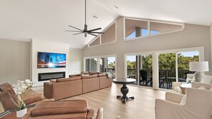 A spacious living room with a large sofa, a dining table, and a TV mounted on the wall. - Tabby Cottage: 3  BR, 3.5  BA House in Jekyll Island, Sleeps 6 (Jekyll Island)