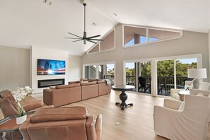 A spacious living room with a large sofa, a dining table, and a TV mounted on the wall. - Tabby Cottage: 3  BR, 3.5  BA House in Jekyll Island, Sleeps 6 (Jekyll Island)