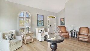 A living room with a round table, two leather chairs, a white armchair, and a wooden cabinet. - Tabby Cottage: 3  BR, 3.5  BA House in Jekyll Island, Sleeps 6 (Jekyll Island)
