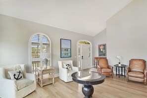 A living room with a round table, two leather chairs, a white armchair, and a wooden cabinet. - Tabby Cottage: 3  BR, 3.5  BA House in Jekyll Island, Sleeps 6 (Jekyll Island)