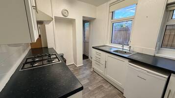 A kitchen with a gas stove, a sink, white cabinets, and a window.