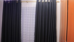 A room with a wooden wardrobe, a window with black curtains, and a sheer curtain partially covering the window. - 1-bed Apartment Sleeps 2 in Nairobi - Free Parking (Nairobi)