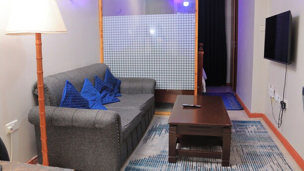 A room with a sofa, a table, a lamp, a TV, and a tiled partition. - 1-bed Apartment Sleeps 2 in Nairobi - Free Parking (Nairobi)