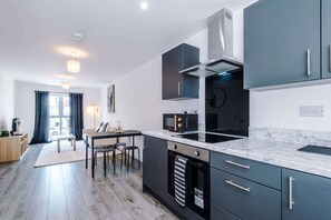 A modern kitchen with dark cabinets, a marble countertop, and a built-in oven. - Stylish 1BDR Hospitals Nearby (Liverpool)