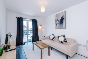 A modern living room with a sofa, a coffee table, a TV, and a painting on the wall. - Modern and Stylish Flat - 1BDR (Liverpool)