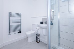 A modern bathroom with a toilet, sink, and glass shower enclosure. - Modern and Stylish Flat - 1BDR (Liverpool)