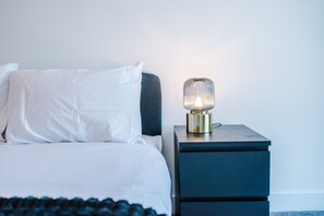 A bed with white linens, a dark headboard, and a bedside table with a lamp. - Modern and Stylish Flat - 1BDR (Liverpool)