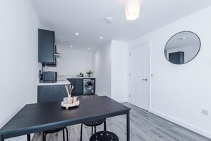 A modern kitchen with a built-in oven, microwave, and washing machine. There is a dining table with chairs and a small side table with a vase and candles. - Modern and Stylish Flat - 1BDR (Liverpool)