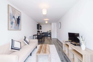 A modern living room with a sofa, coffee table, TV, and kitchen in the background. - Stylish 1BDR Hospitals Nearby (Liverpool)