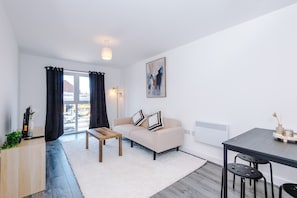 A modern living room with a sofa, coffee table, and a dining area with a table and chairs. - Modern and Stylish Flat - 1BDR (Liverpool)
