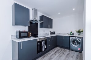Una cocina moderna con gabinetes grises, microondas integrado, estufa, lavaplatos y lavadora.