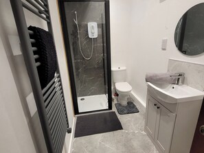 Ein modernes Badezimmer mit Duschkabine aus Glas, Toilette, Waschbecken und Spiegel.
