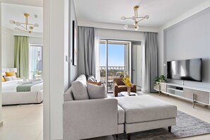A modern hotel room with a sofa, a TV, a balcony, and a view of the city. - Silkhaus Furnished 1BR Stay in Downtown Views II (Dubai)