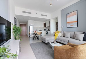 A modern living room with a sofa, coffee table, and a dining area with chairs and a table. - Silkhaus Furnished 1BR Stay in Downtown Views II (Dubai)