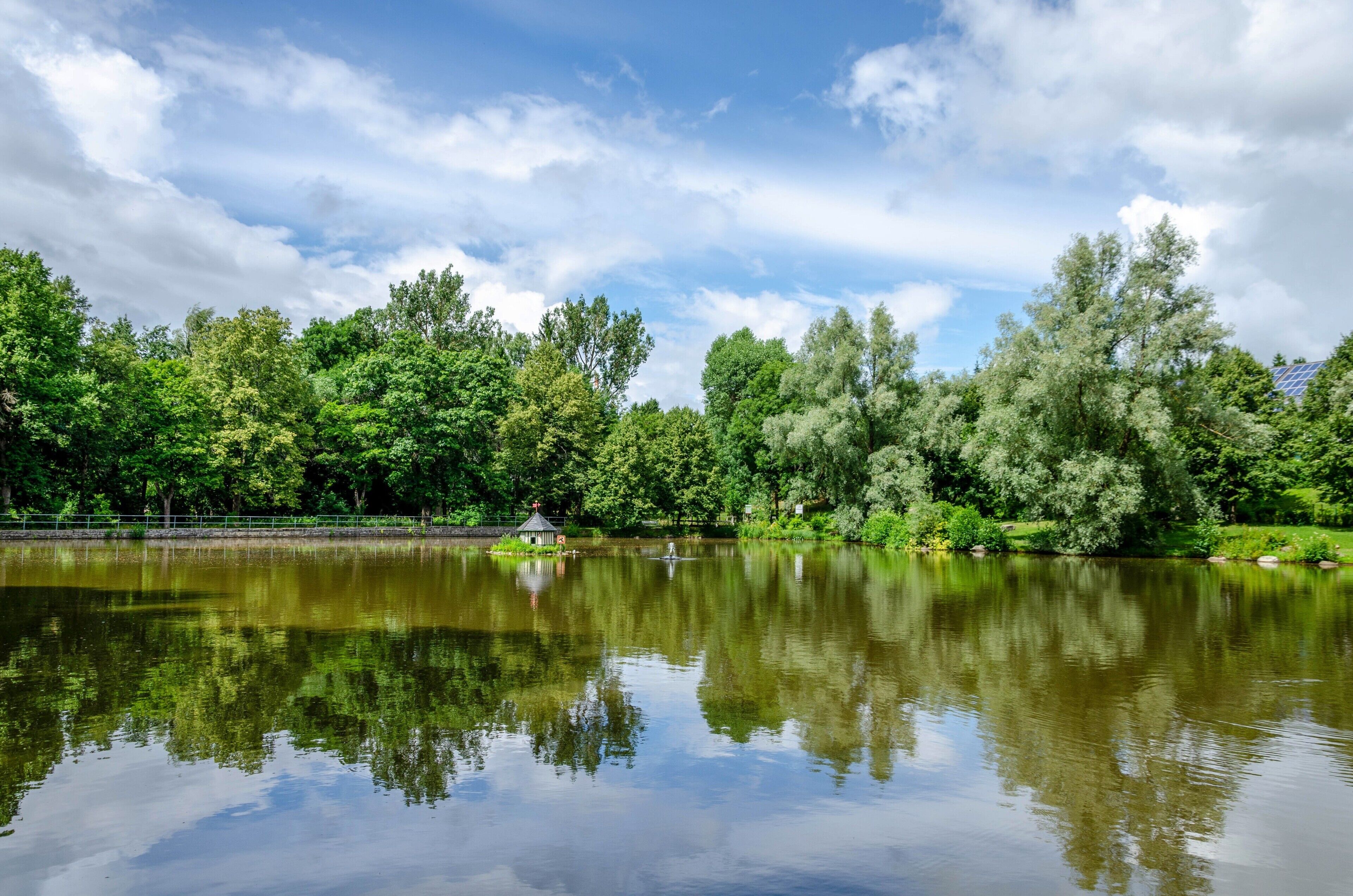 A tranquil lake surrounded by lush greenery and a gazebo.