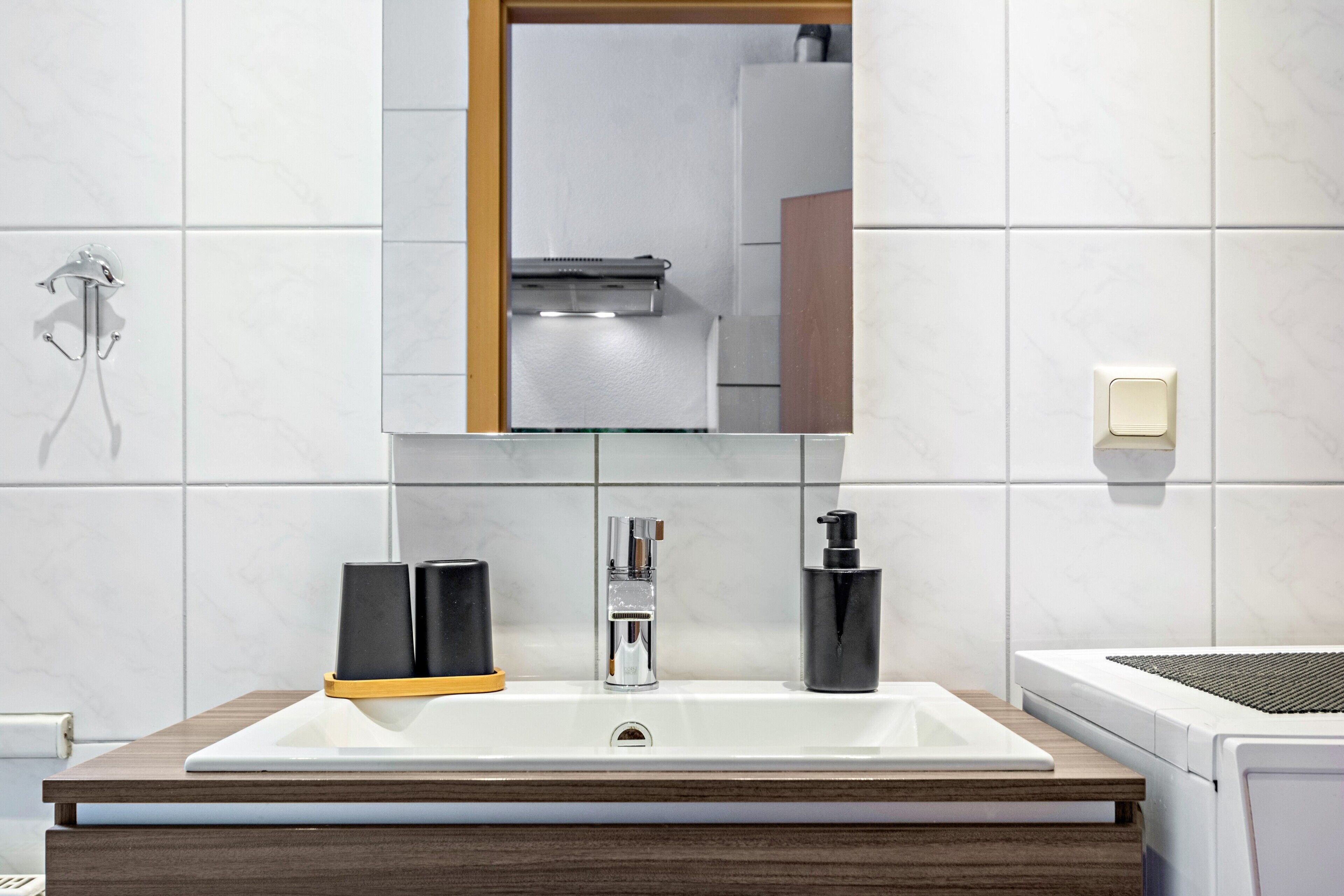 A modern bathroom with a large mirror, a white sink, a faucet, and a soap dispenser.