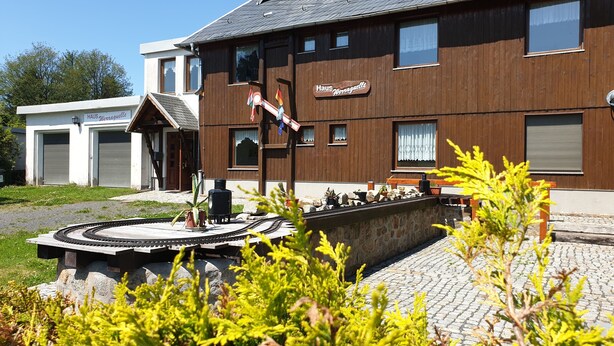 Ein zweistöckiges Gebäude mit Holzfassade, einem Schild mit der Aufschrift 'Haus Wurgauselle' und einer kleinen Außenbereich-Sitzgelegenheit mit Tisch und Stühlen.