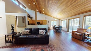A spacious living area with a leather sofa, wooden flooring, and large windows. - Sunriver Retreat with Access to Exclusive Golf (Sunriver)