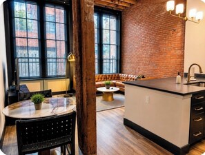 Una cocina con pared de ladrillo, un ventanal amplio, una mesa redonda con sillas y una isla integrada con un lavaplatos.