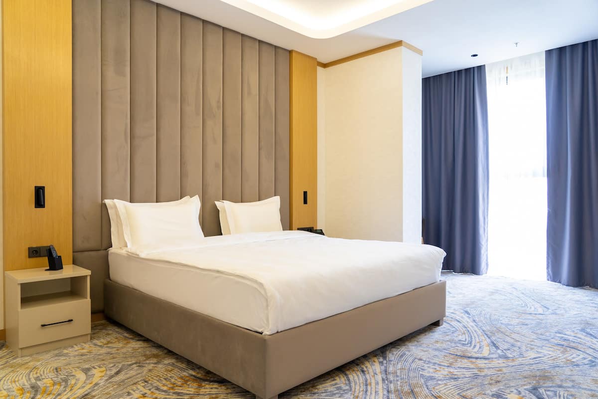 Una habitación de hotel con una cama grande, una mesita de noche y un ventanal con cortinas.