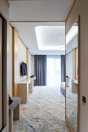 A hotel room with a bed, a desk, a mirror, a television, and a bathroom. - Grand Afrosiyob Hotel (Tashkent)