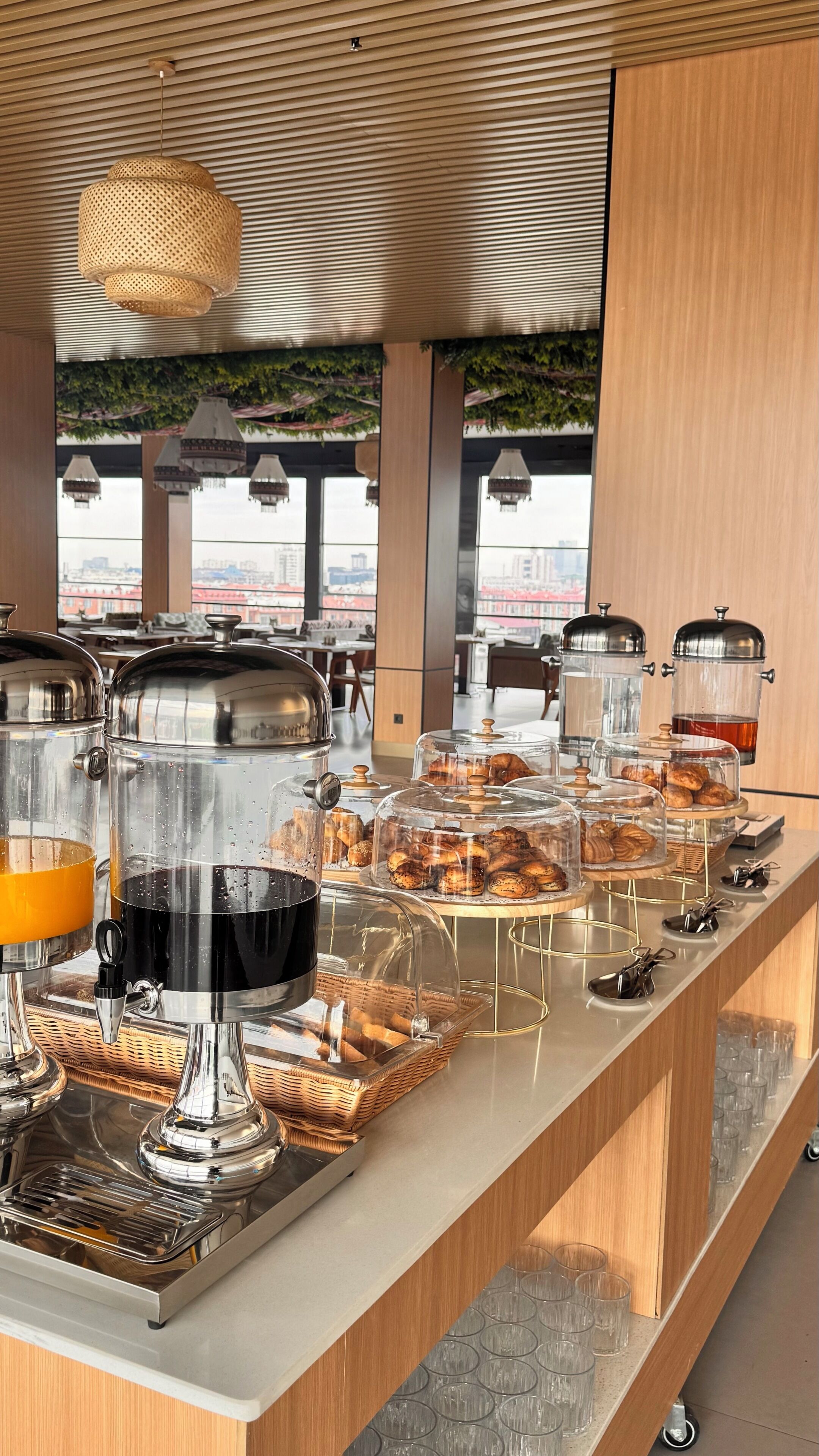 A breakfast buffet with various food items and beverages, a wooden ceiling, and a view of buildings in the background.