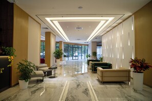 Een hotel lobby met een marmeren vloer, een zithoek en potplanten.