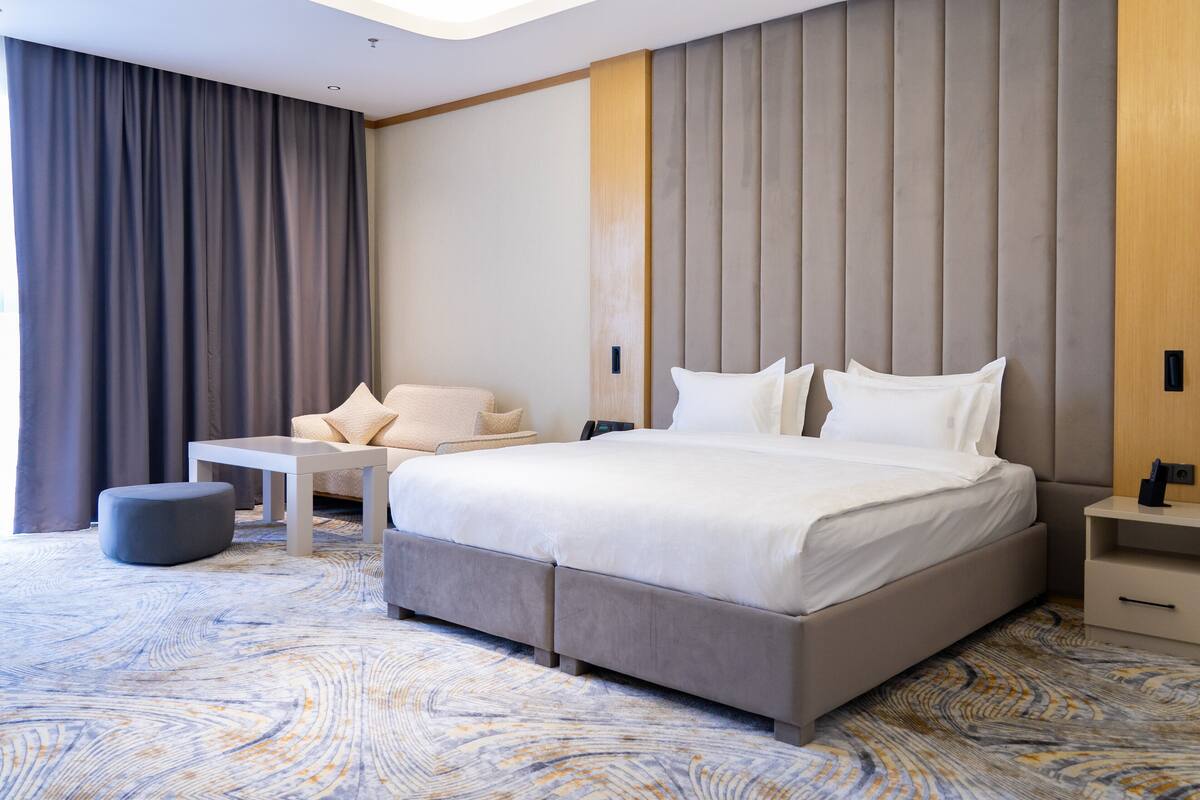 Habitación de hotel moderna con una cama grande, un sofá pequeño, una mesa de centro y una mesita de noche.