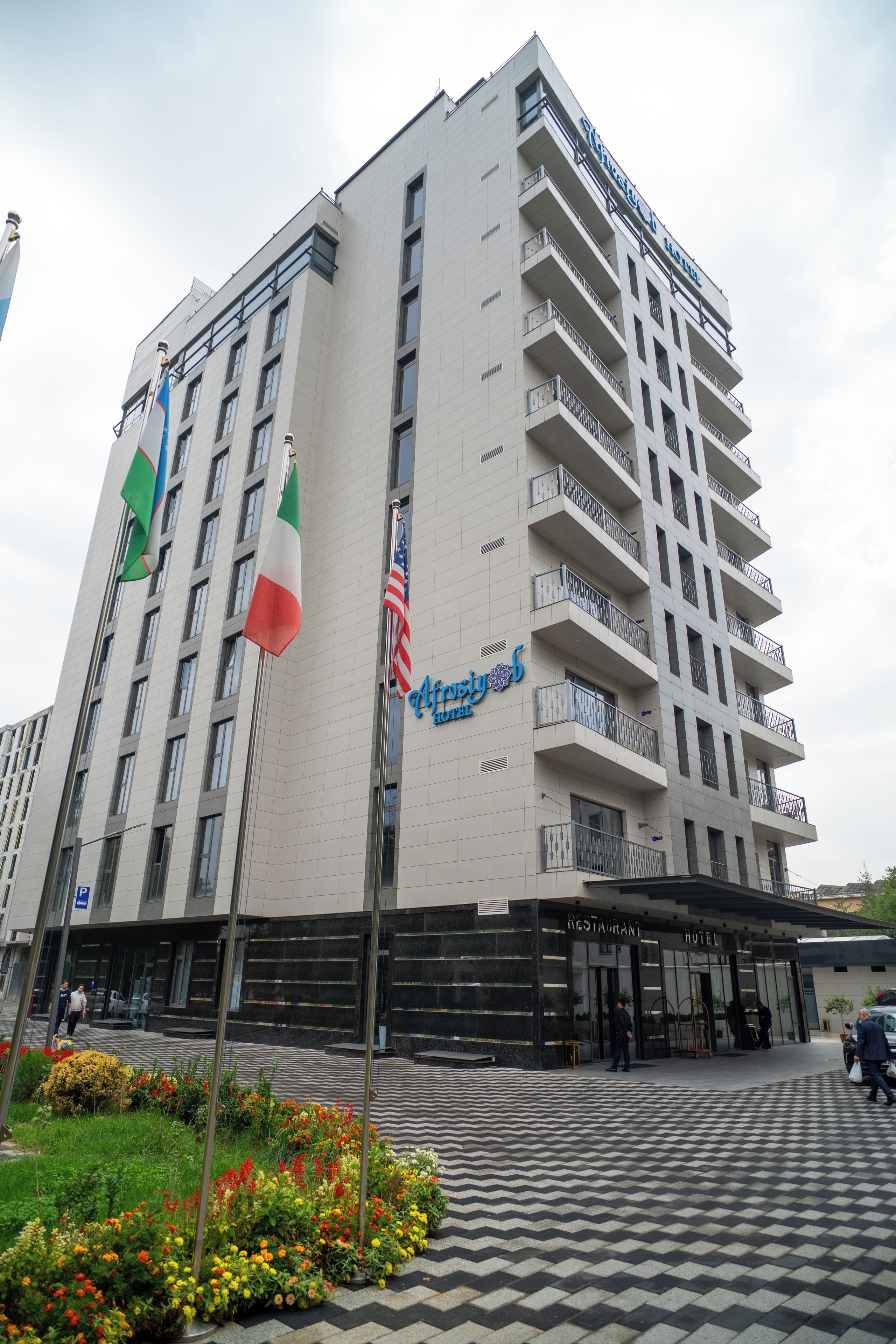 Un hotel de varios pisos, un asta con banderas y un adoquinado a cuadros en la fachada.
