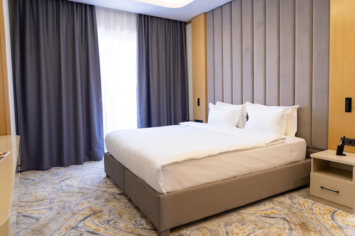 Una habitación de hotel con una cama grande, una mesita de noche y una ventana con cortinas.