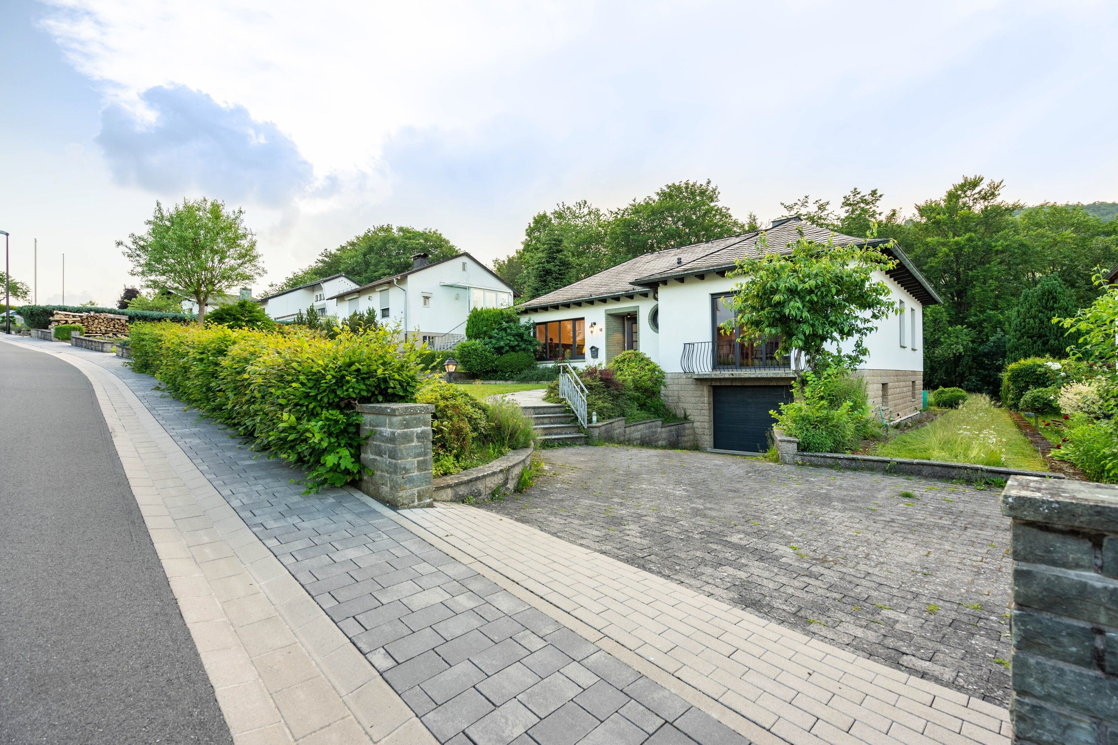 A residential street with houses, paved sidewalks, and greenery.