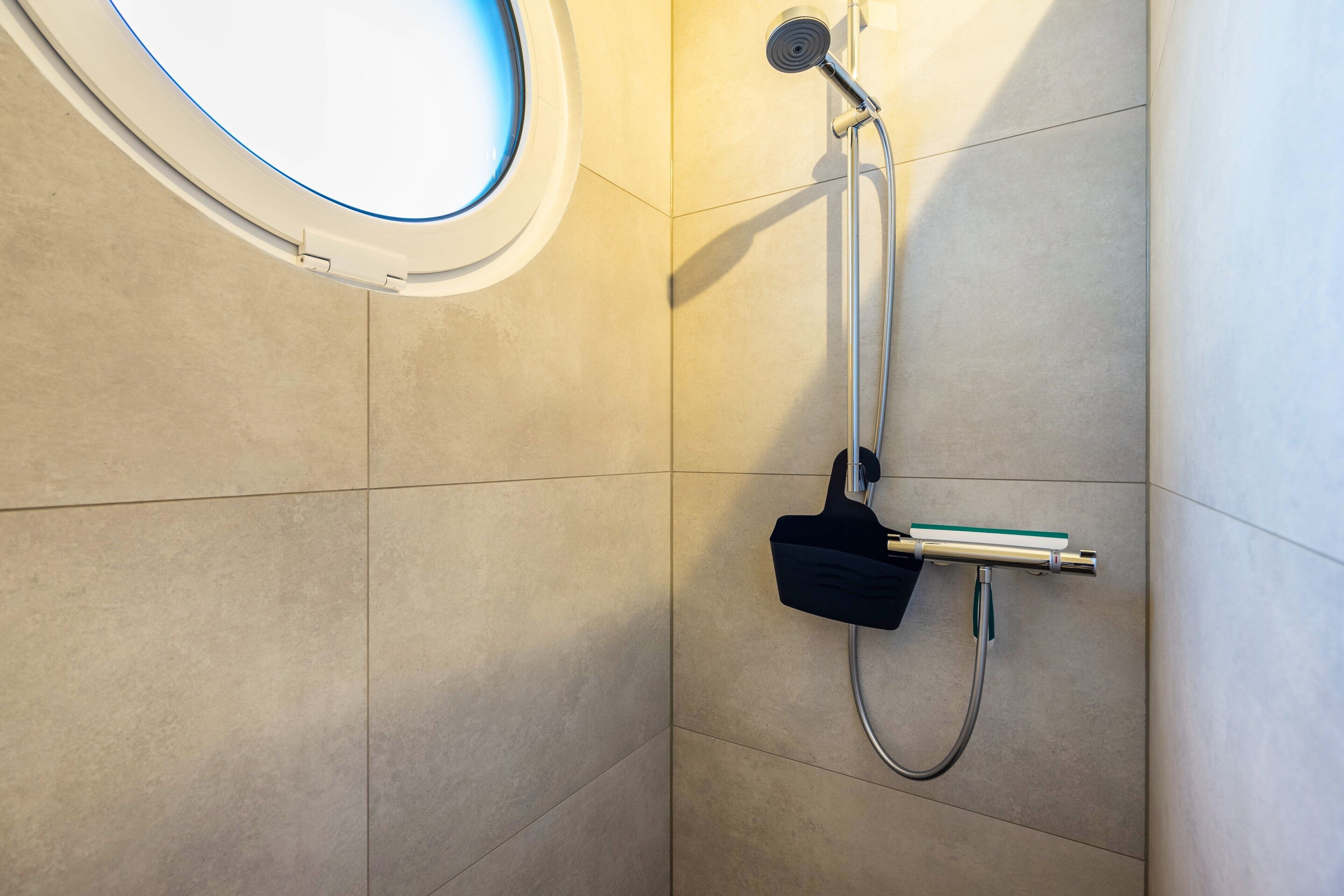 Eine Dusche mit Duschbrause, Seifenspender und einem Fenster mit blauer Tönung.