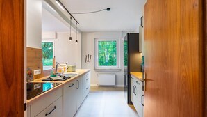 Moderni keittiö, jossa on valkoiset kaapit, puinen työtaso ja näkymä vehreään maisemaan.