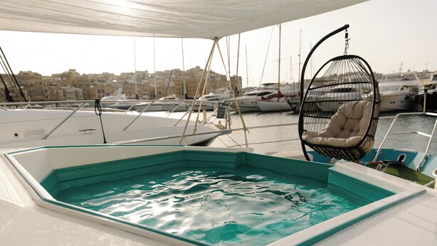 Área de piscina com uma cadeira suspensa, rodeada por barcos e vista para uma marina.