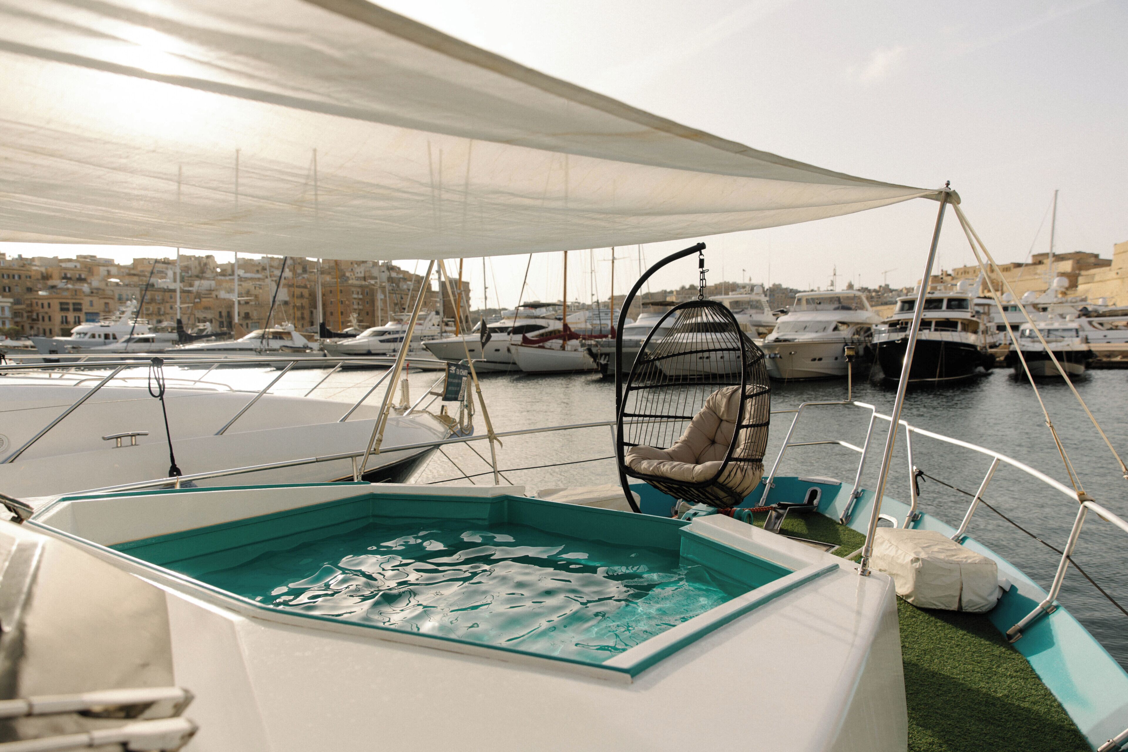 A marina with boats docked, a covered seating area with a cushioned chair, and a pool.