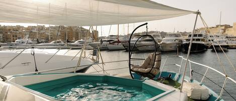 A marina with boats docked, a covered seating area with a cushioned chair, and a pool.