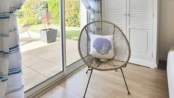 Une chaise en osier avec un coussin, une porte-fenêtre coulissante et une plante en pot.