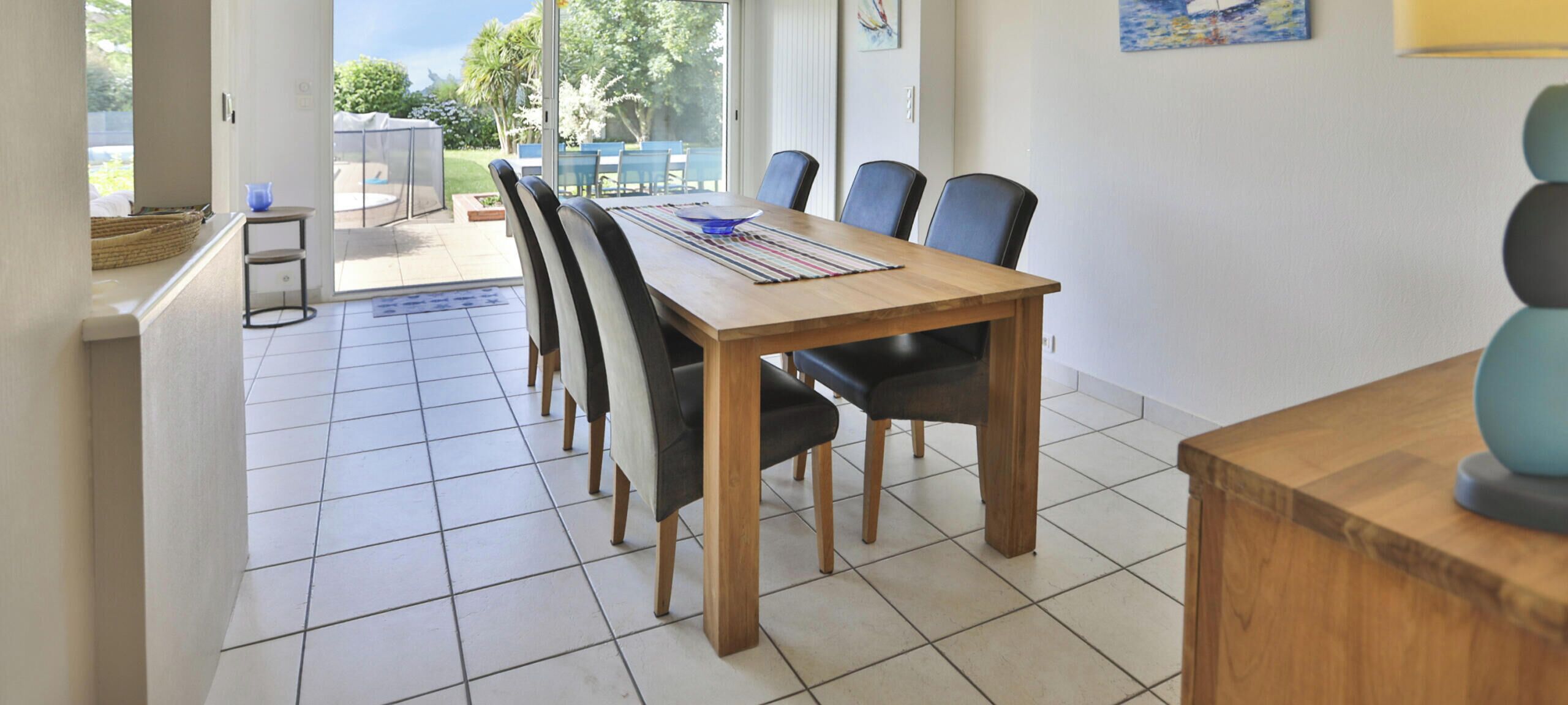 Un espace repas avec une table et des chaises en bois, un sol carrelé et une vue sur l’extérieur.