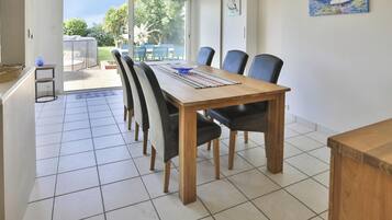 Un espace repas avec une table et des chaises en bois, un sol carrelé et une vue sur l’extérieur.