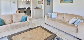 Ein Wohnzimmer mit zwei beigefarbenen Sofas, einem Couchtisch mit Muster, einem Essbereich mit Stühlen und Kunstwerken an den Wänden.