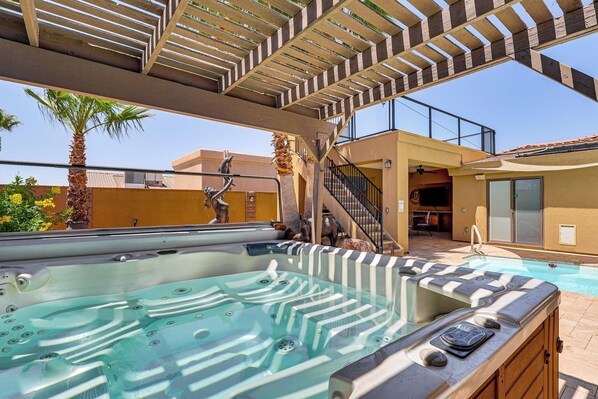A hot tub with a wooden pergola overhead, a pool, and a staircase leading to an upper level.