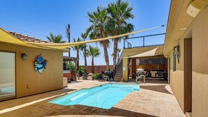 Ein Schwimmbecken mit gefliestem Deck, Palmen und einer überdachten Terrasse.