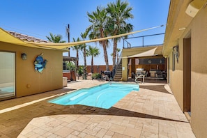 A swimming pool with a tiled deck, palm trees, and a covered patio area.